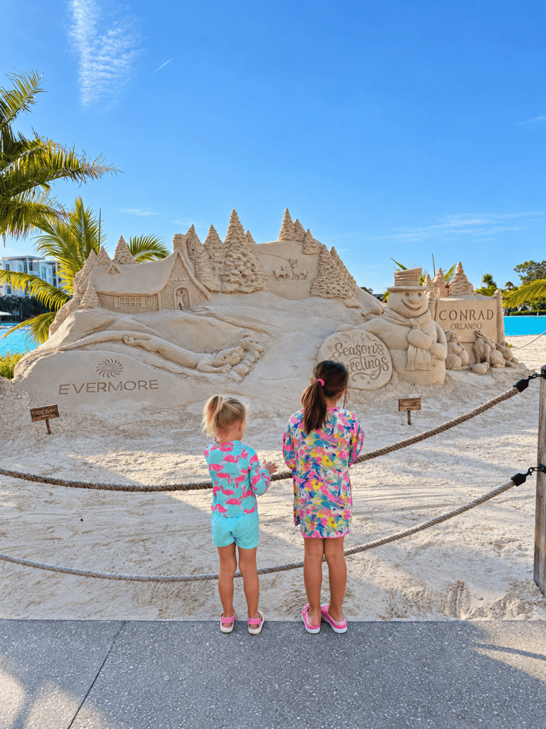 Two children admiring a holiday sand sculpture beside the lagoon (Evermore Bay) at Evermore Orlando Resort