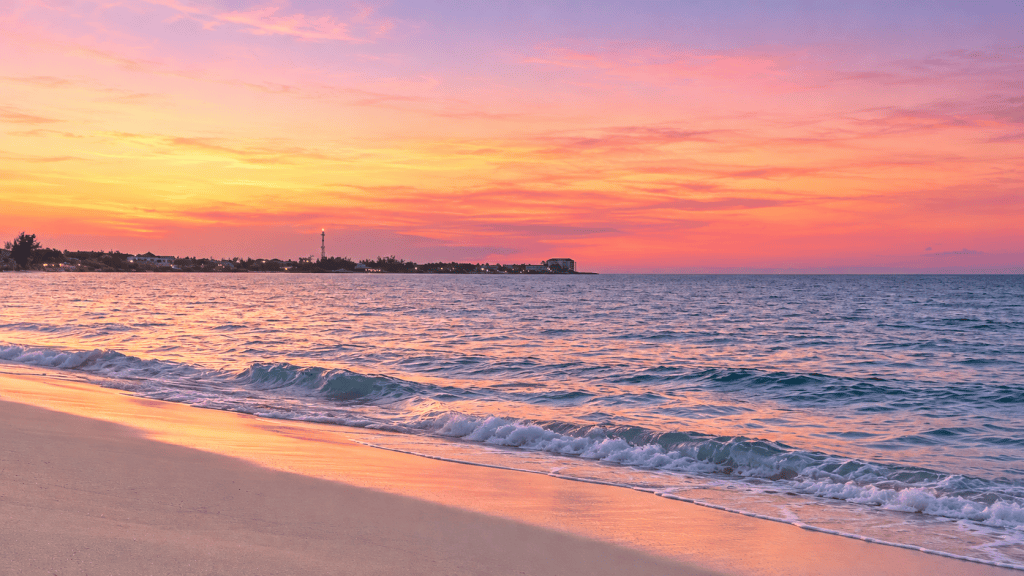 Pink and peach sunset over a sandy beach and gentle ocean waves in Nassau, Bahamas.