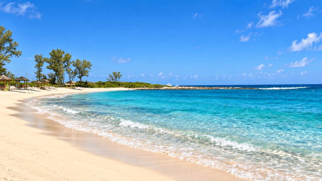 White-sand beach with turquoise water and beach cabanas on Sandals Royal Bahamian’s private island in Nassau, Bahamas.